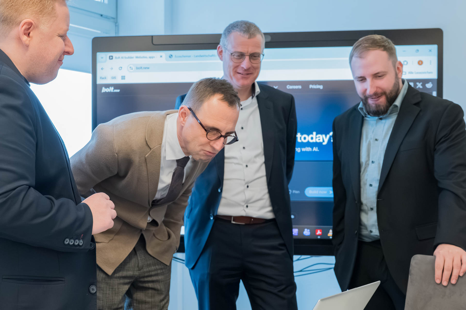Vier Männer schauen interessiert in einen Laptop